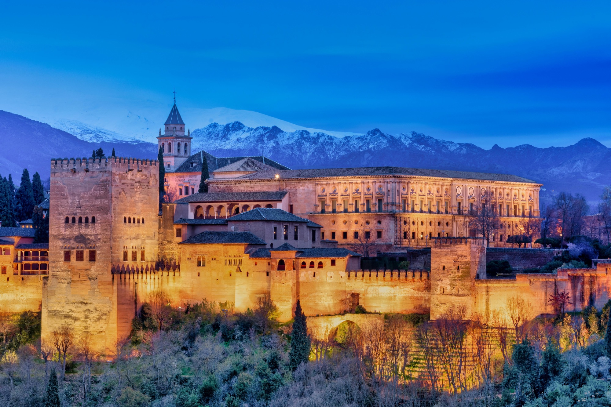 La Alhambra iluminada al anochecer con Sierra Nevada nevada detrás